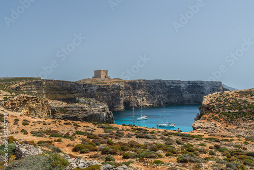 The small island of Comino with yachts on the Crystal Lagoon overlooked by the small watchtower called Saint Mary's Tower built in 1618.