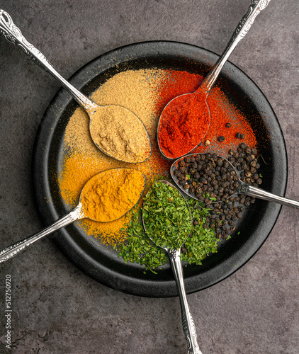 Assorted of colorful spices (red pepper powder, turmeric powder, black pepper, dried parsley leaves, and kaempferia galanga powder) with a dramatic concept of background and varied angles. photo