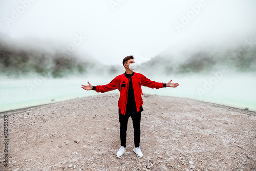 Fotografiet young man in red bomber jacket standing at kawah putih sulfer lake in Bandung