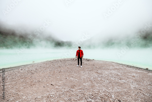 wide angle young man in red bomber jacket standing at kawah putih sulfer lake in Bandung photo