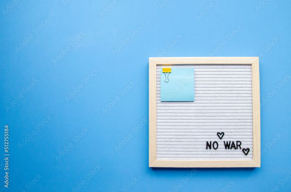 Flatlay composition with a blue background, a letter board in a wooden frame with the phrase NO WAR and small hearts, blue sticker