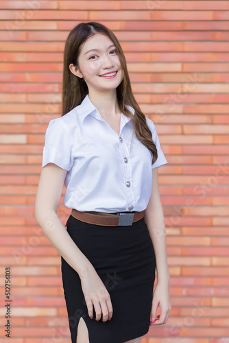 Portrait of an adult Thai student in university student uniform. Asian beautiful girl standing with her smiling happily on a brick background.