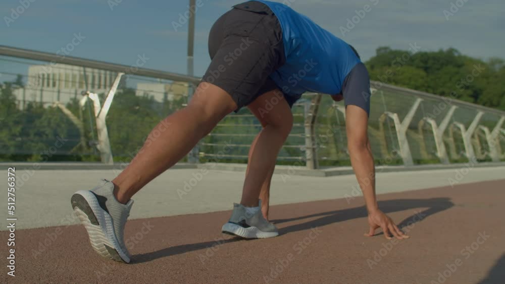 Rear view of determined active fit African athlete in sports jersey crouched down ready for start and running on track, while exercising cardio workout in city at daybreak. Rear view of determined active fit African athlete in sports jersey crouched down ready for start and running on track, while exercising cardio workout in city at daybreak.