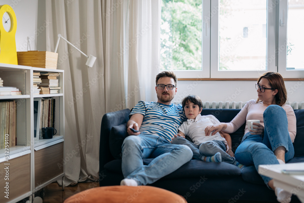 Family of three sitting on a sofa and watching TV together at home