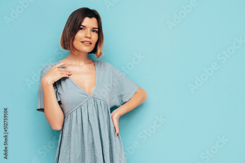 Portrait of young beautiful smiling female in trendy summer dress. Sexy carefree woman posing near blue wall in studio. Positive model having fun and going crazy. Cheerful and happy