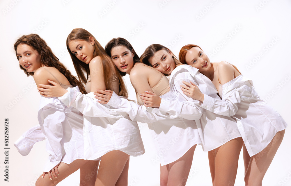 Group of young beautiful women posing in beige cotton underwear and shirt, leaning at each other isolated over white studio background Group of young beautiful women posing in beige cotton underwear and shirt, leaning at each other isolated over white studio background