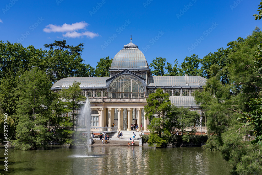Crystal Palace. Building located in the Retiro Park in Madrid with its glass windows surrounded by trees and green vegetation on a sunny day and some clouds in the sky, in Spain. Europe. Photography.