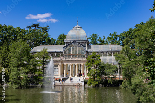 Crystal Palace. Building located in the Retiro Park in Madrid with its glass windows surrounded by trees and green vegetation on a sunny day and some clouds in the sky, in Spain. Europe. Photography.