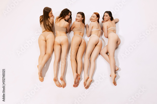 Top view portrait of five woman lying on belly. Image of slender, smooth female legs and buttocks in underwear isolated over grey background