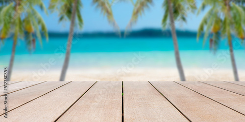 Empty old wooden table in front of blurred background of sea, sand, palm tree, mountain and tropical beach at summer vacation and travel concept with copy space.