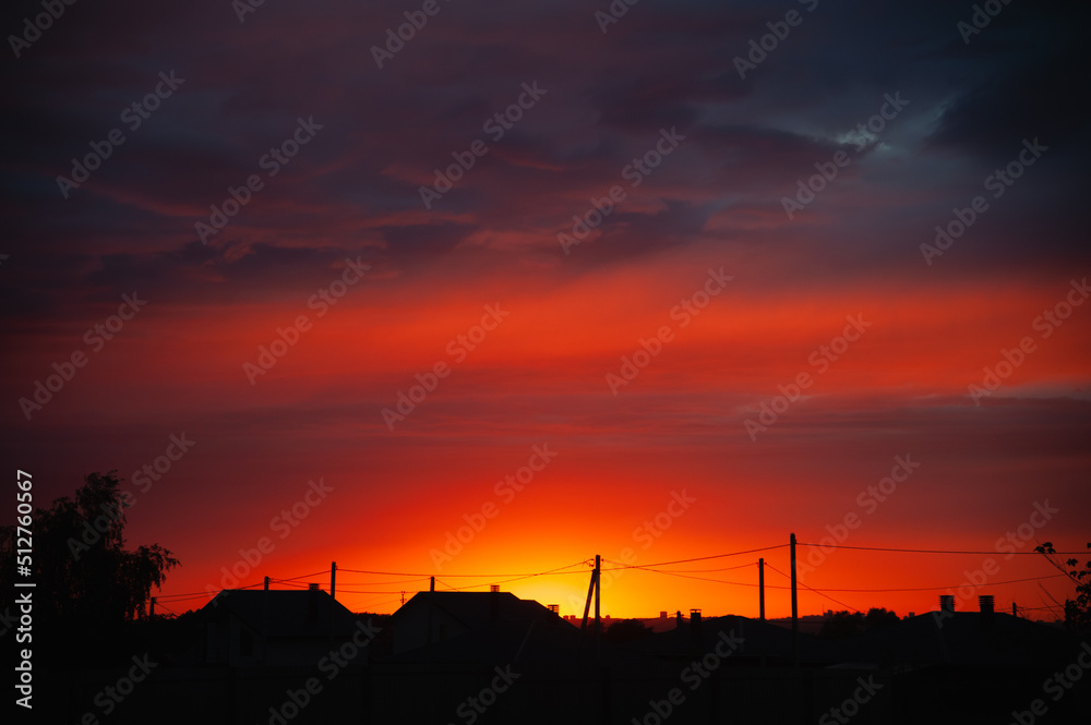 Rural houses against the backdrop of a fiery sunset. Evening landscape