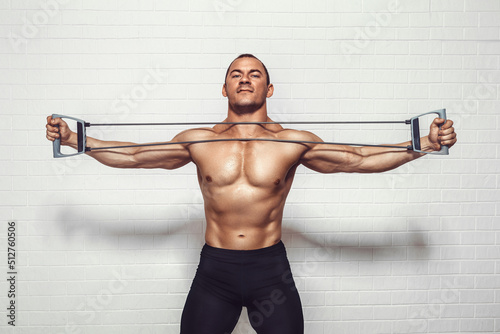Handsome young sportsman exercising using expander while standing against white background