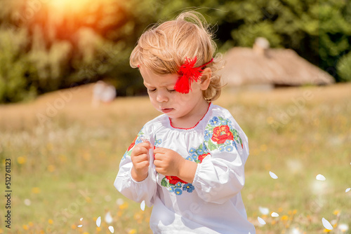 Fotografie, Tablou Funny little Ukrainian Caucasian girl in a shirt with embroidery playing in nature where wild flowers