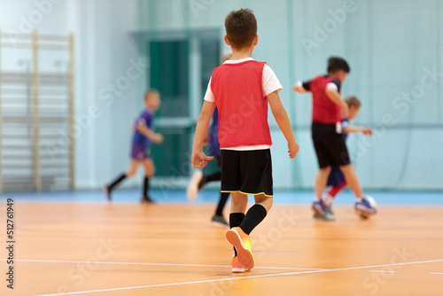 Football training for children. Indoor soccer young player with a soccer ball in a sports hall. Sport background. Elementary age kids kicking indoor soccer