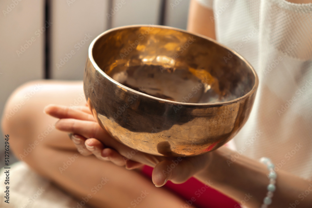 Close-up of young woman playing on a singing tibetian bowl.Relaxation and meditation.Sound therapy,alternative medicine.Buddhist healing practices.Selective focus.