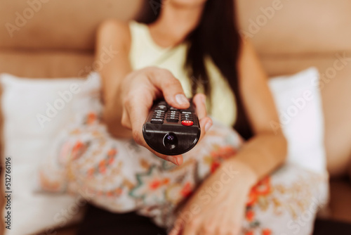 Portrait of young woman holding tv remote control, sitting on couch, watching TV at home. 