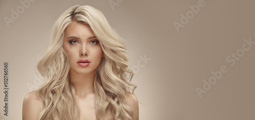 Much attractive blonde woman with long healthy curly hair on beige isolated with free copy space photo