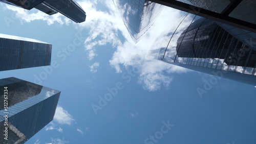 Bottom view of tops of glass skyscrapers on background blue sky. Action. Modern architecture of business centers reflecting blue sky. Dizzying view of modern glass skyscrapers