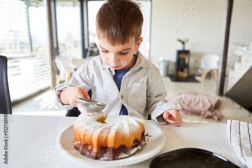 Kleiner Junge streut Puderzucker über den Marmorkuchen photo