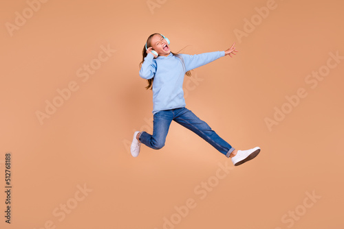 Full body portrait of overjoyed carefree person jump arm touch headphones isolated on beige color background
