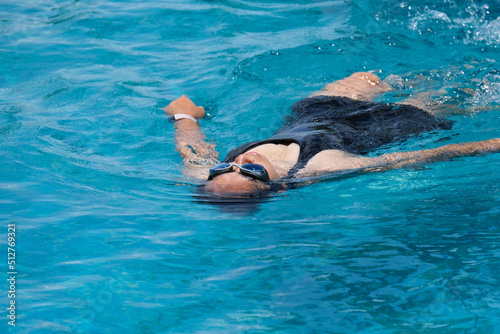 Beautiful young asian woman happy and smile in swimming pool. Asian woman in swimsuit is swimming in the blue clean water of the swimming pool for exercise. Travel and summer vacation concept.