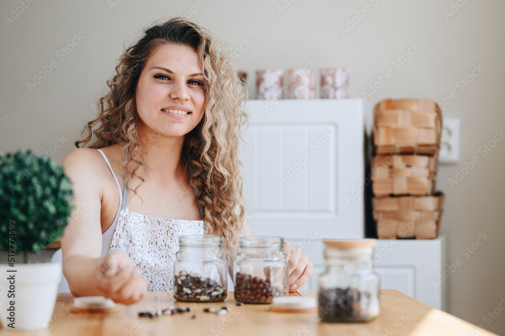housewife sorts out beans in Kitchen at Table. Young Curly Woman Smiling Sitting at Table. housewife sorts out beans in Kitchen at Table. Young Curly Woman Smiling Sitting at Table.