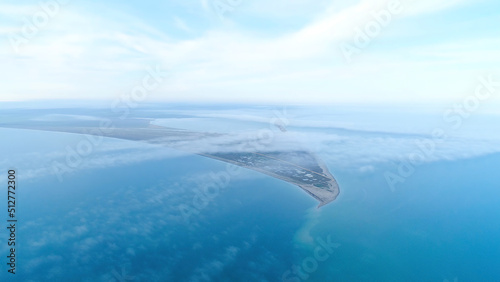 Top view of coast among sea on background of sky horizon. Shot. The highest view in sky among clouds on blue sea and triangular shore