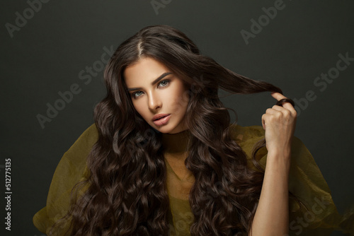 Brunette beauty. Healthy young woman with long wavy hair touсhing her hair curl on black. Fashion, hair care and beauty concept.