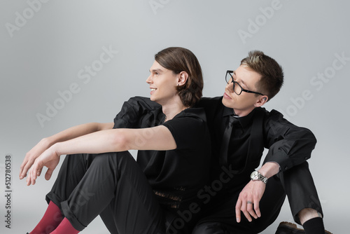 Man in formal wear looking at smiling boyfriend on grey background.