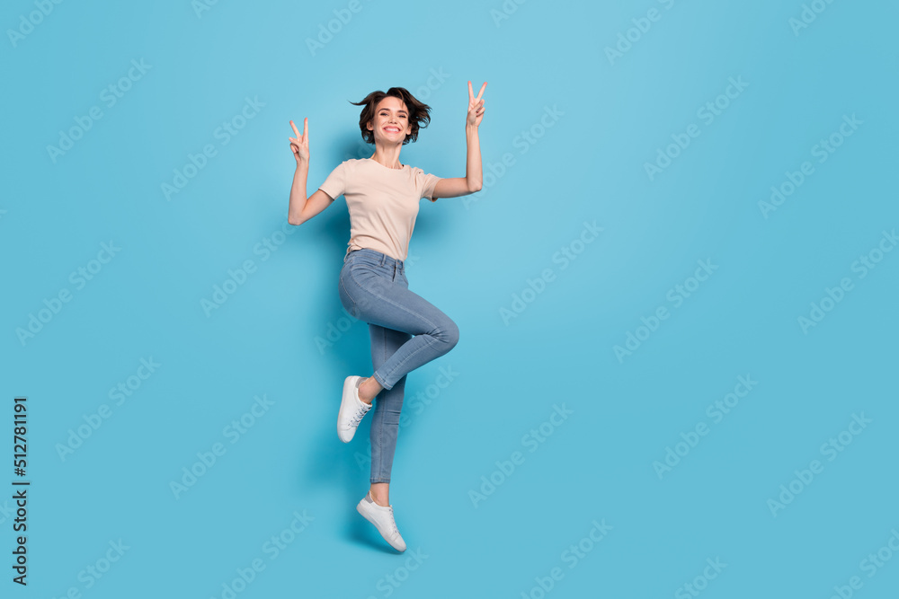 Full length photo of shiny cute lady dressed beige t-shirt jumping high showing v-signs empty space isolated blue color background