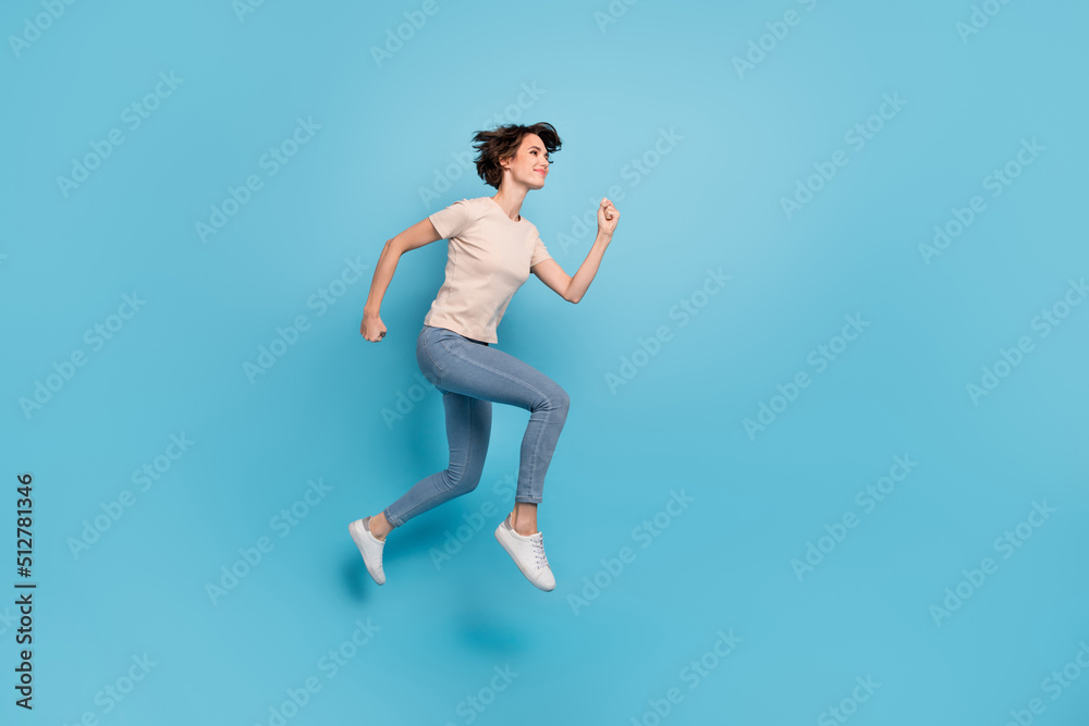 Full length photo of cute sweet lady dressed beige t-shirt jumping high running fast empty space isolated blue color background