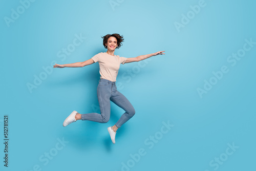 Full length photo of funny shiny lady dressed beige t-shirt jumping arms sides empty space isolated blue color background