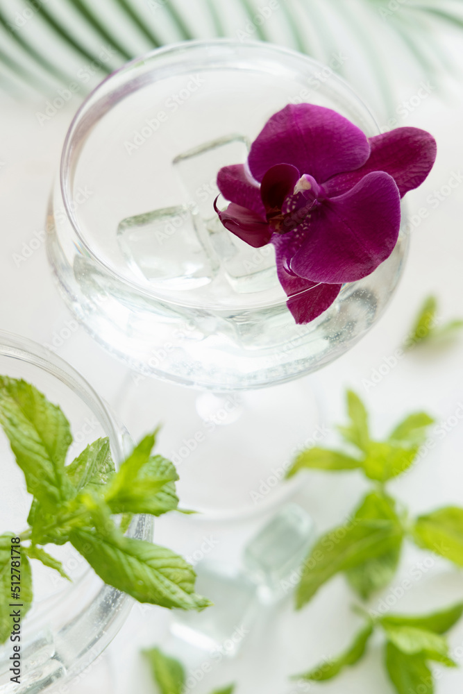 Transparent cocktail in a glass decorated with purple orchid flowers and mint leaves close up Transparent cocktail in a glass decorated with purple orchid flowers and mint leaves close up