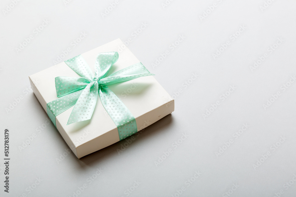 wrapped Christmas or other holiday handmade present in white paper with green ribbon on colored background. Present box, decoration of gift on colored table, top view with copy space wrapped Christmas or other holiday handmade present in white paper with green ribbon on colored background. Present box, decoration of gift on colored table, top view with copy space