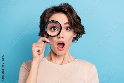 Photo of young impressed young lady using magnifying glass play detective catch spy isolated on blue color background photo