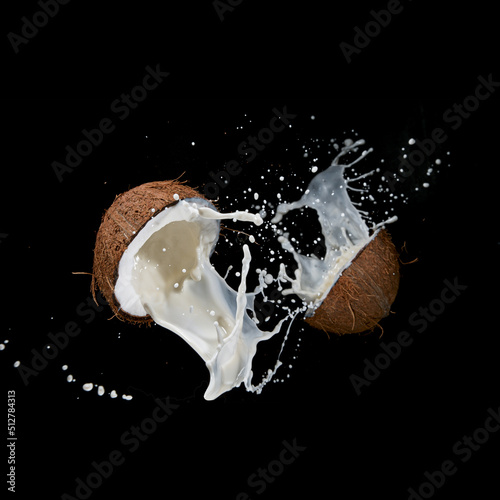 Cracked Coconut with milk splash flying in the air, isolated on black.