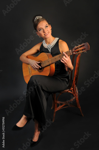 Girl with a guitar in a black dress on a black background