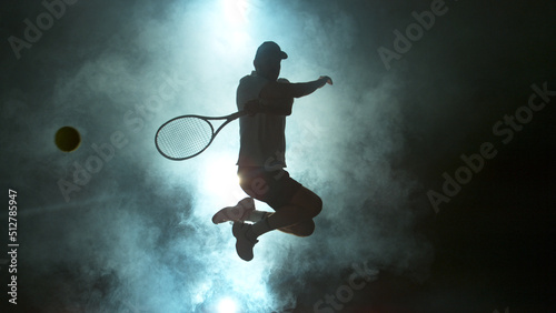 Jumping Player Hitting Tennis Ball with Atmosferic Smoke on Background