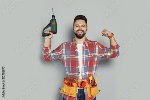 Young worker with power drill and tool belt on grey background photo