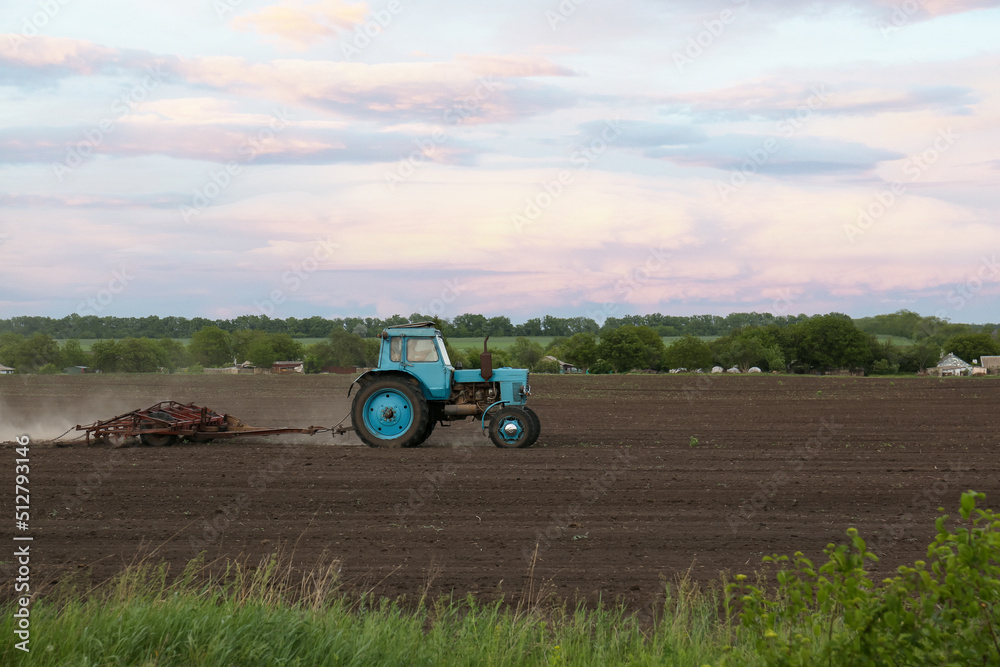 Obraz premium Tractor plowing agricultural field under cloudy sky