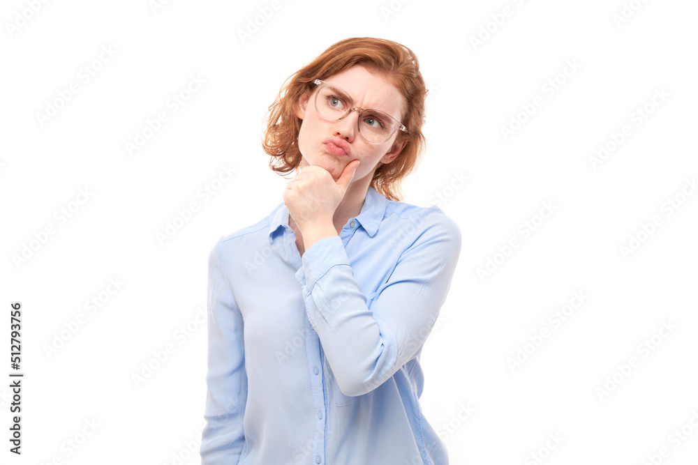 Smart redhead girl in glasses and business shirt holding chin thinks doubts, makes decision isolated on white studio background Smart redhead girl in glasses and business shirt holding chin thinks doubts, makes decision isolated on white studio background