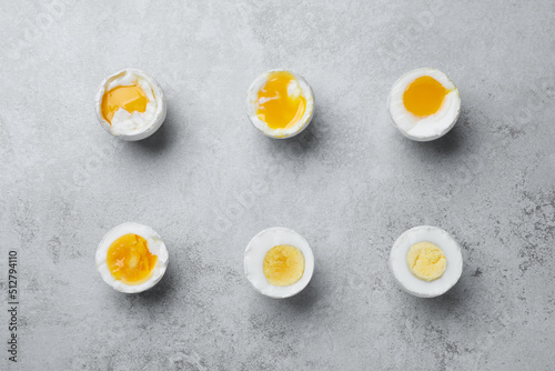 Different readiness stages of boiled chicken eggs on light grey table, flat lay