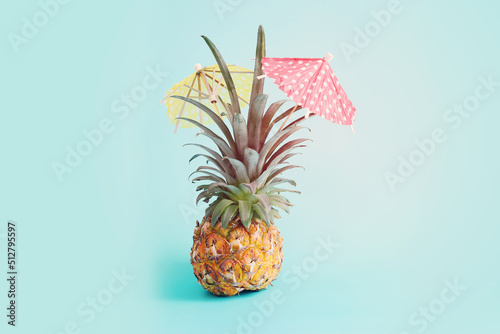 Image with ripe pineapple with parasol over blue background. Summer holidays and tropical theme
