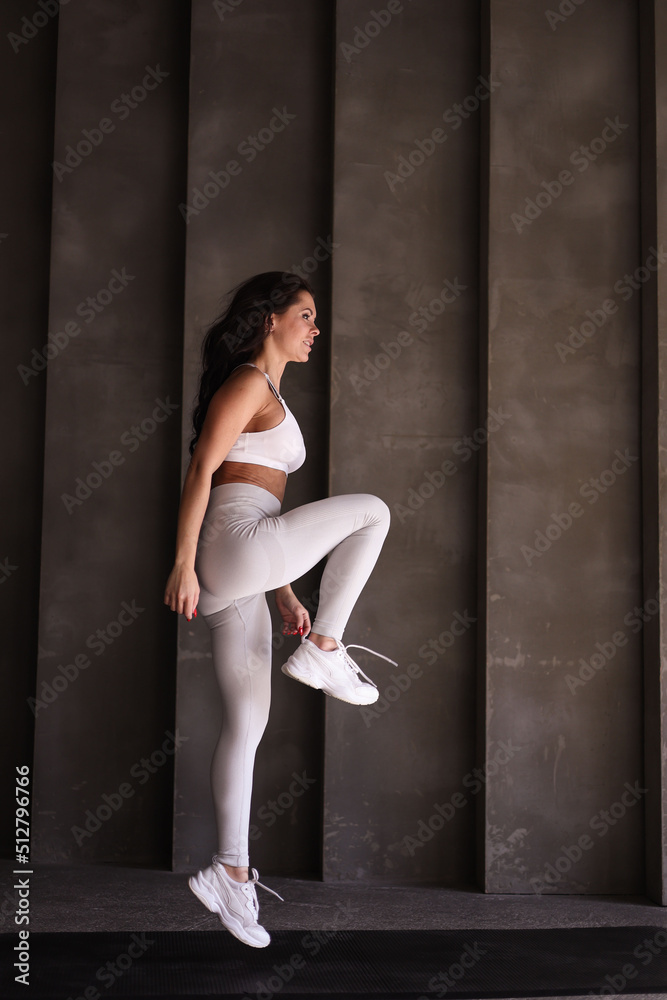 Beautiful strong muscular woman practicing sports in gym. Healthy woman trainer in white sportswear jump alone. Fit girl doing cardio exercises alone. Beautiful strong muscular woman practicing sports in gym. Healthy woman trainer in white sportswear jump alone. Fit girl doing cardio exercises alone.