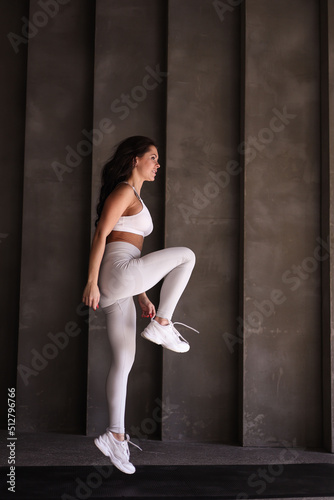 Beautiful strong muscular woman practicing sports in gym. Healthy woman trainer in white sportswear jump alone. Fit girl doing cardio exercises alone. 