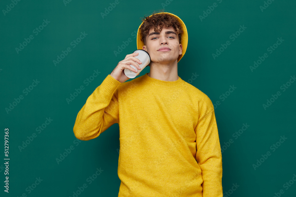a joyful man stands on a green background in a yellow T-shirt and hat holding a cardboard coffee cup in his hand. Horizontal photo for inserting an advertising layout
