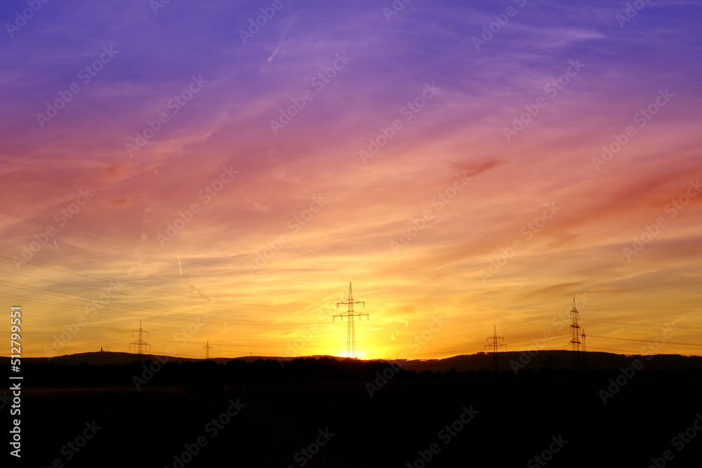 beautiful dramatic landscape, sky with airplane trail lines, power towers, field in evening in rays of sunset, concept of beauty of nature, modern energy, technology, black hills at bottom
