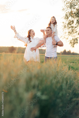 Family walks on meadow and father carries daughter on his shoulders.