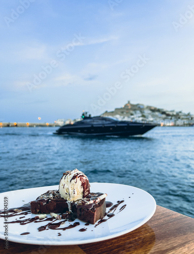 Chocolate brownie with ice cream close up and yacht in the background. Romantic restaurant dinner in new Marina Botafoch in Ibiza, with view on the sea and Ibiza old town on the other side of the bay photo