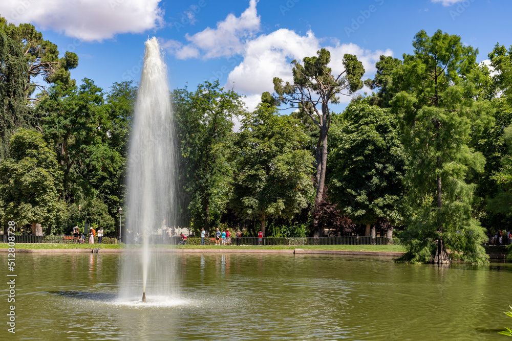 Font. Water fountain in a pond in a Madrid park, with tall green trees in the background on a clear day in Spain. Europe. Horizontal photography.